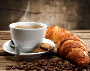 Photo représentant une tasse de café fumante et un croissant.