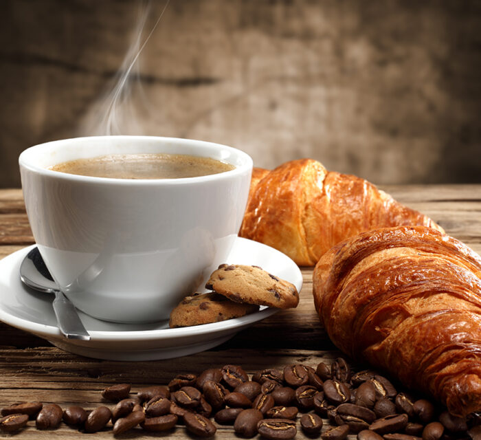 Photo représentant une tasse de café fumante et un croissant.