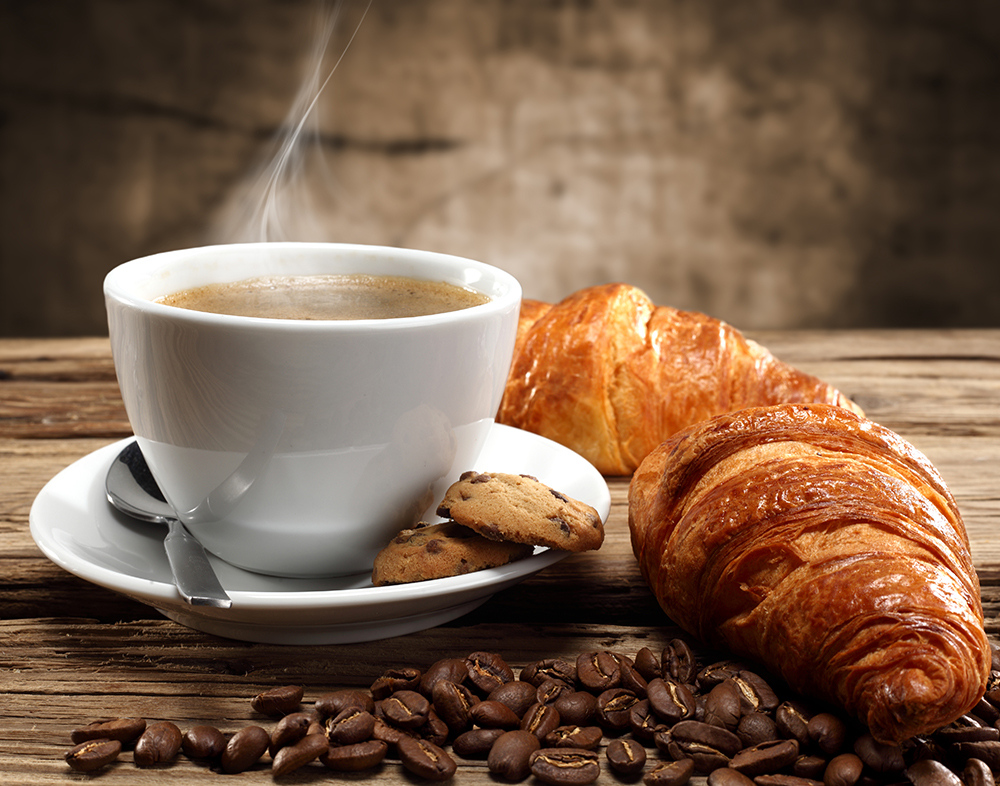 Photo représentant une tasse de café fumante et un croissant.