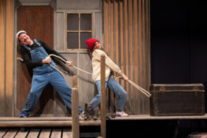 Un comédien et une comédienne en salopette sur scène avec un chien tirent sur une corde