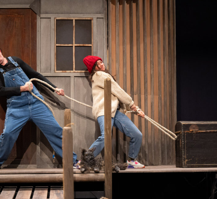 Un comédien et une comédienne en salopette sur scène avec un chien tirent sur une corde