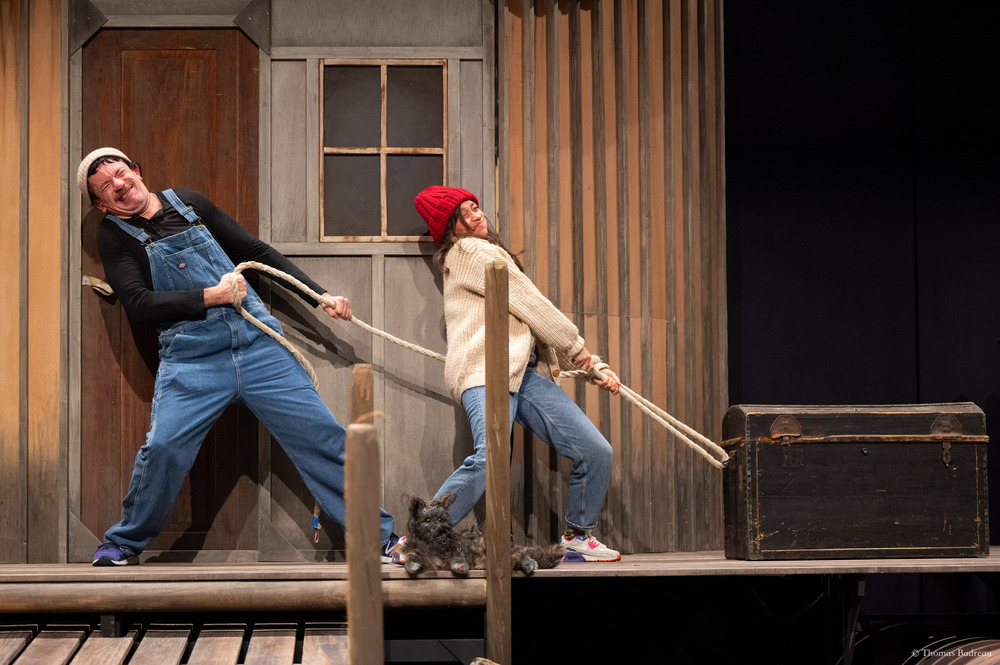 Un comédien et une comédienne en salopette sur scène avec un chien tirent sur une corde