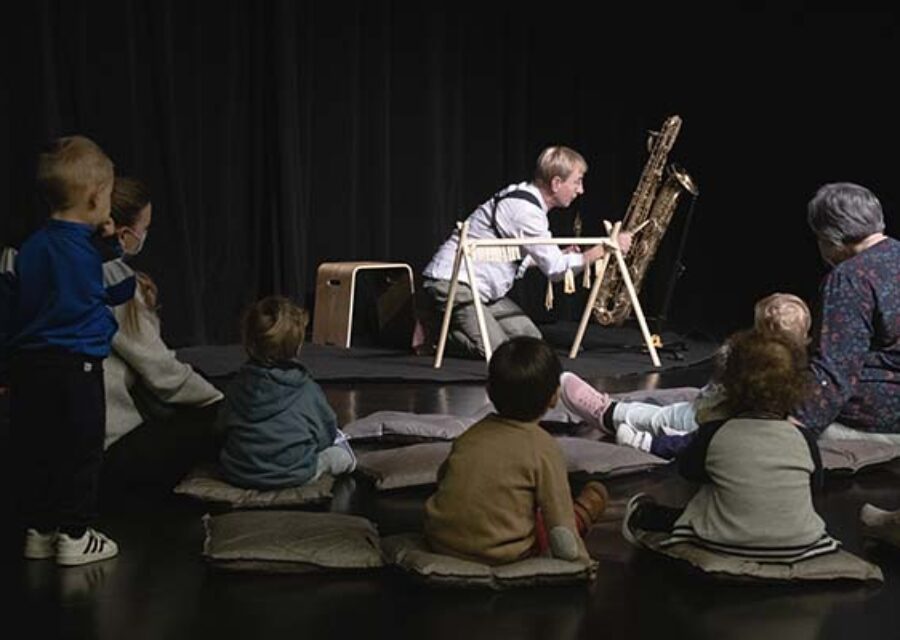 Des enfants et des adultes devant un musicien avec un saxophone baryton.
