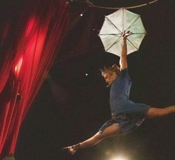 Une fil de fériste saute en grand écart avec une ombrelle à la main.