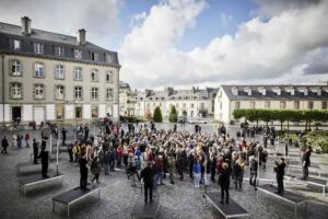 Les 20 sonneurs installés en rond sur une place avec le public debout au milieu.