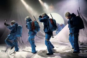 Le décor représente une montagne enneigée et 4 comédiens en tenue bleue d'alpinistes traversent la scène.