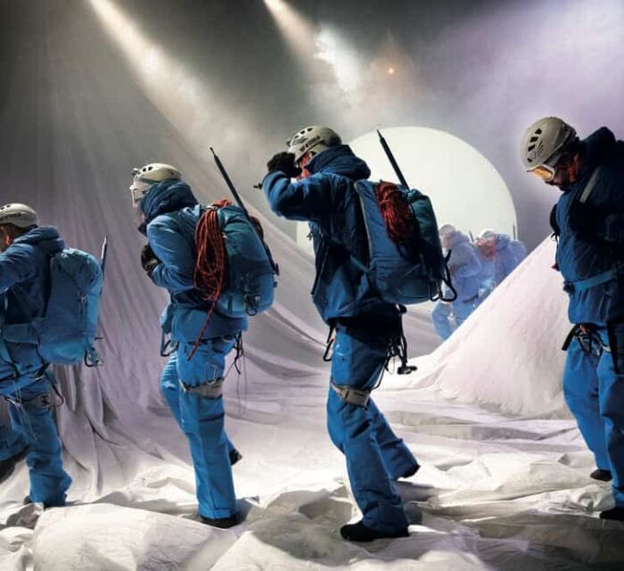 Le décor représente une montagne enneigée et 4 comédiens en tenue bleue d'alpinistes traversent la scène.