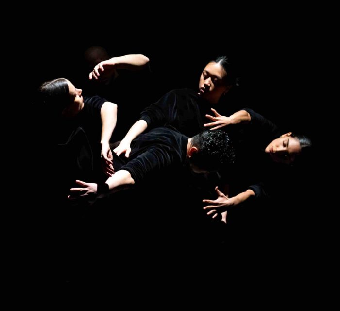 Les visages et les mains de danseurs et danseuses dans un clair-obscur.