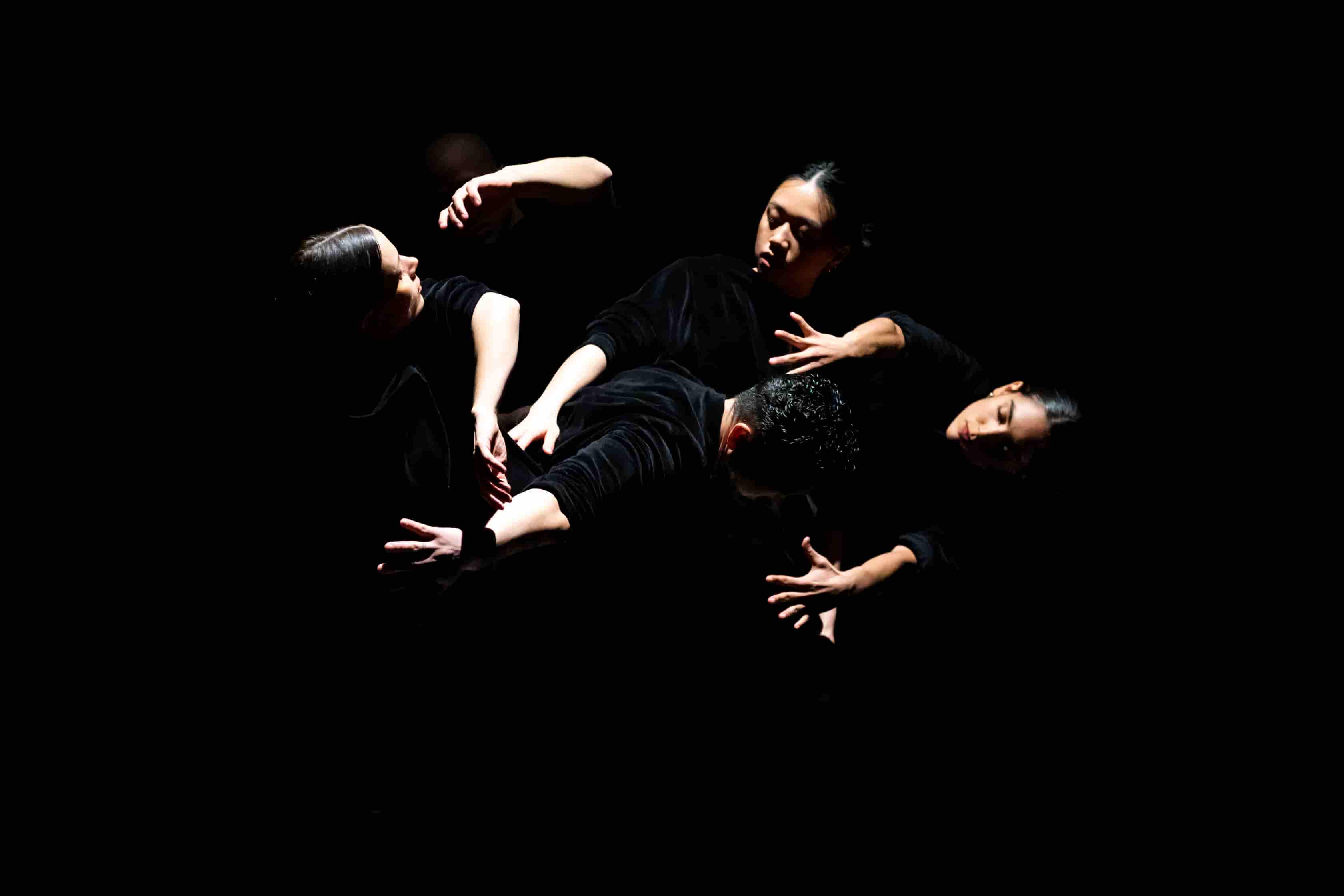 Les visages et les mains de danseurs et danseuses dans un clair-obscur.