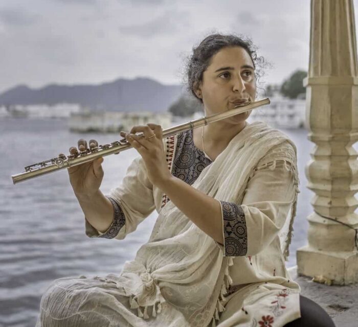 Naïssam Jalal assise de face et jouant de la flûte traversière au bord de l'eau.