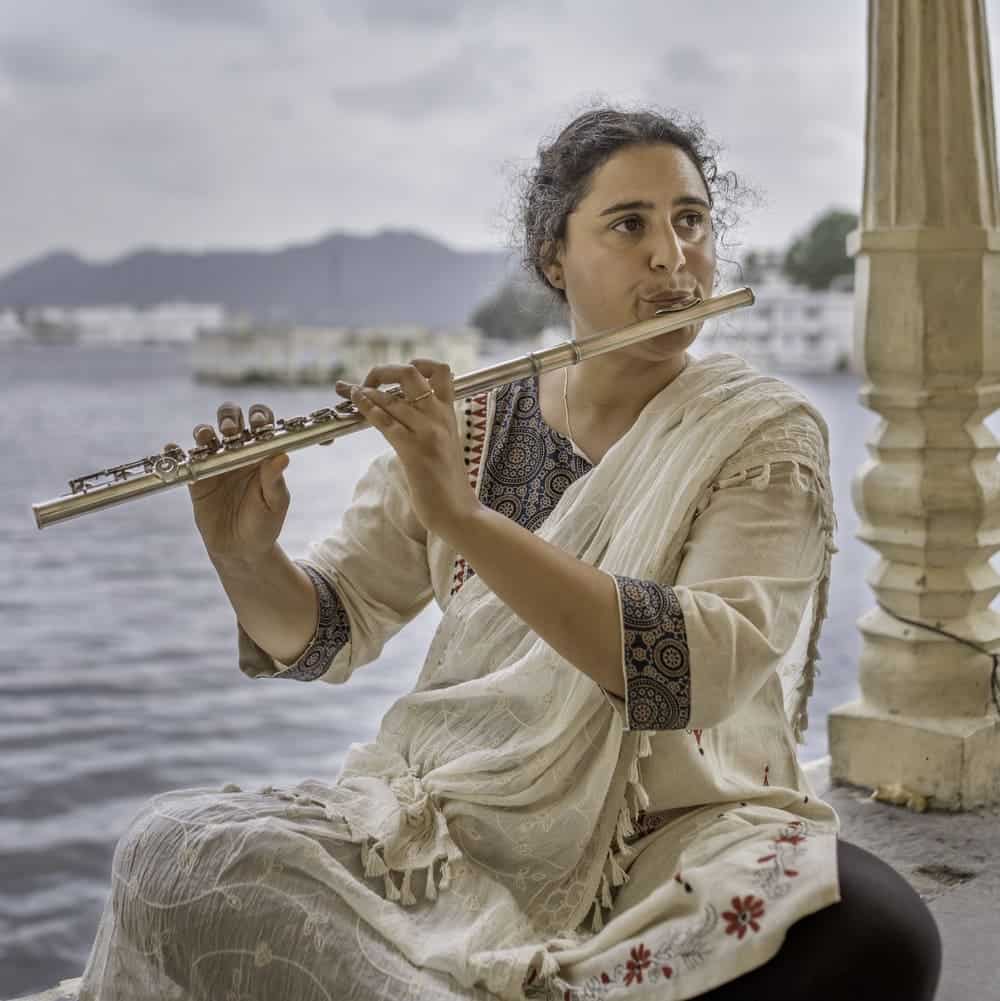 Naïssam Jalal assise de face et jouant de la flûte traversière au bord de l'eau.