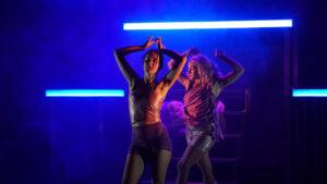 Une jeune femme danse les bras en l'air et les yeux fermés dans une lumière bleutée. Un deuxième personnage apparaît en arrière plan, habillé de la même manière, comme son double.