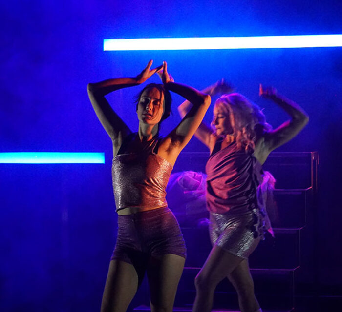 Une jeune femme danse les bras en l'air et les yeux fermés dans une lumière bleutée. Un deuxième personnage apparaît en arrière plan, habillé de la même manière, comme son double.